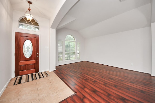 entrance foyer with light wood-style flooring, arched walkways, vaulted ceiling, and baseboards