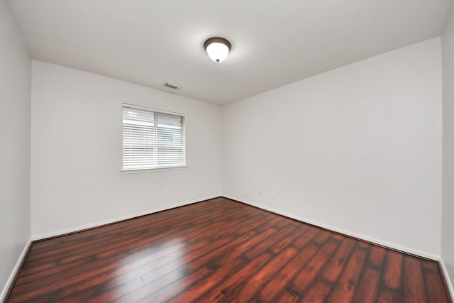 unfurnished room with baseboards, visible vents, and dark wood-style flooring