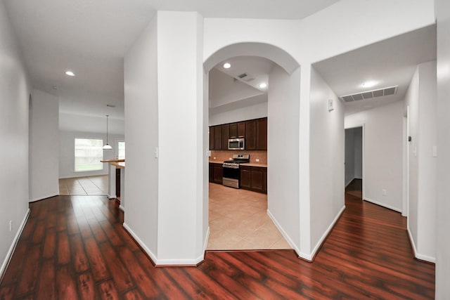 hall with baseboards, visible vents, arched walkways, and wood finished floors