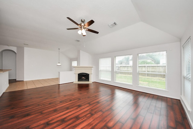 unfurnished living room with visible vents, a fireplace with raised hearth, a ceiling fan, vaulted ceiling, and wood finished floors