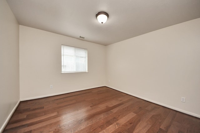 spare room with dark wood finished floors, visible vents, and baseboards