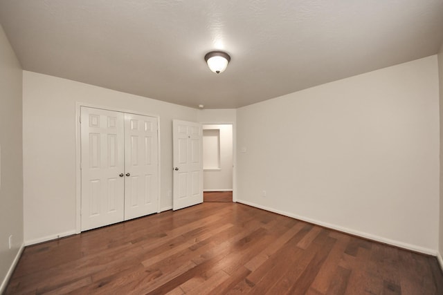 unfurnished bedroom featuring dark wood-type flooring, a closet, and baseboards