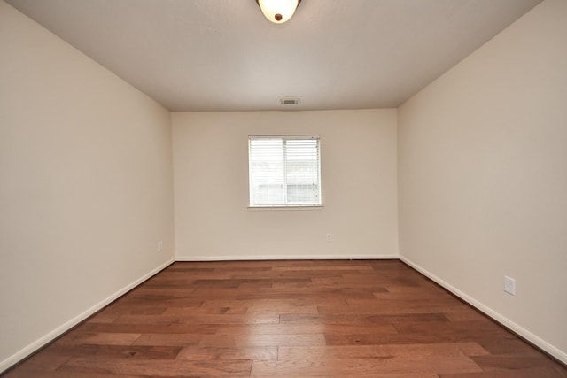 empty room featuring dark wood-style floors, visible vents, and baseboards