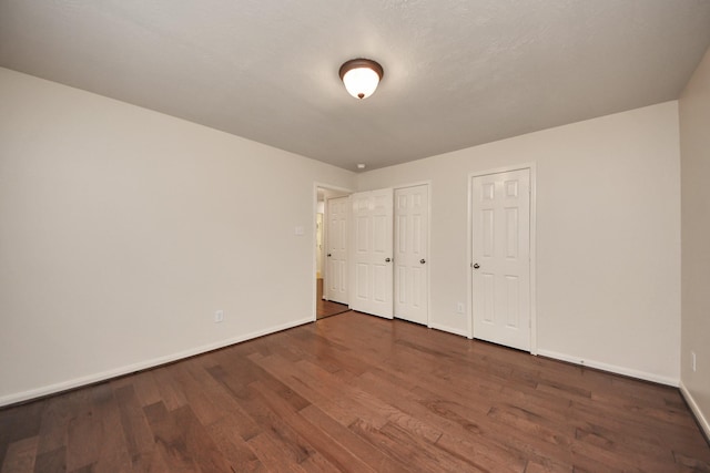 unfurnished bedroom featuring multiple closets, dark wood finished floors, and baseboards