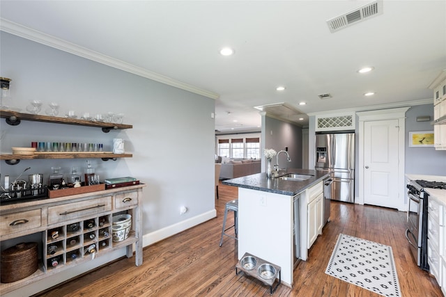 kitchen with appliances with stainless steel finishes, a breakfast bar area, an island with sink, sink, and white cabinetry