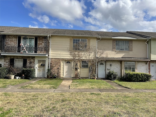 multi unit property with brick siding, a front lawn, and a balcony