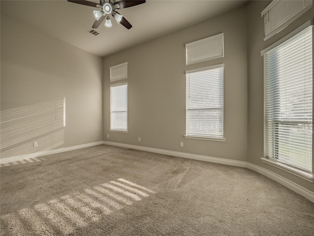 carpeted spare room featuring a ceiling fan, baseboards, visible vents, and a wealth of natural light