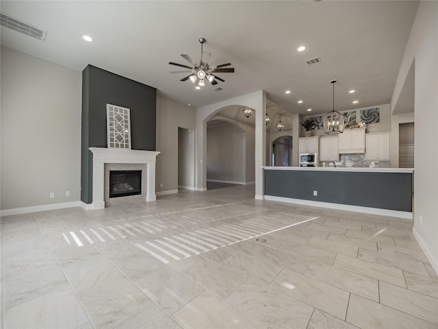 unfurnished living room with recessed lighting, visible vents, a glass covered fireplace, baseboards, and ceiling fan with notable chandelier