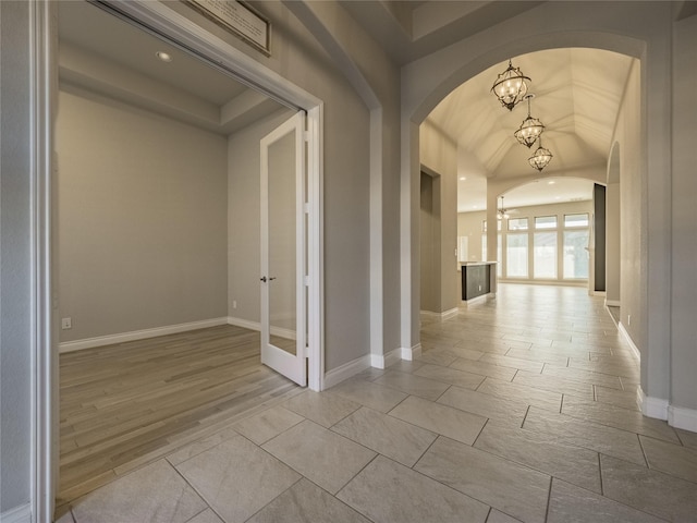 corridor with arched walkways, light wood finished floors, baseboards, and a notable chandelier