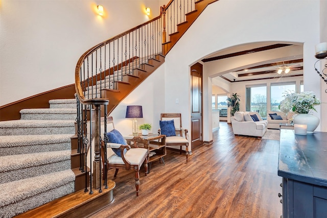 stairs featuring arched walkways, wood finished floors, and beamed ceiling