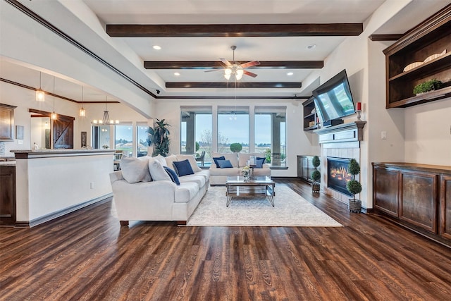 living area with ceiling fan with notable chandelier, dark wood-style flooring, beam ceiling, and a fireplace