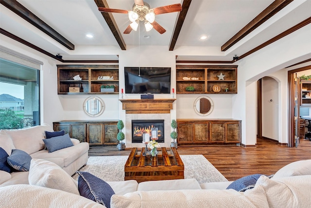 living area featuring a glass covered fireplace, arched walkways, baseboards, dark wood-style floors, and beam ceiling