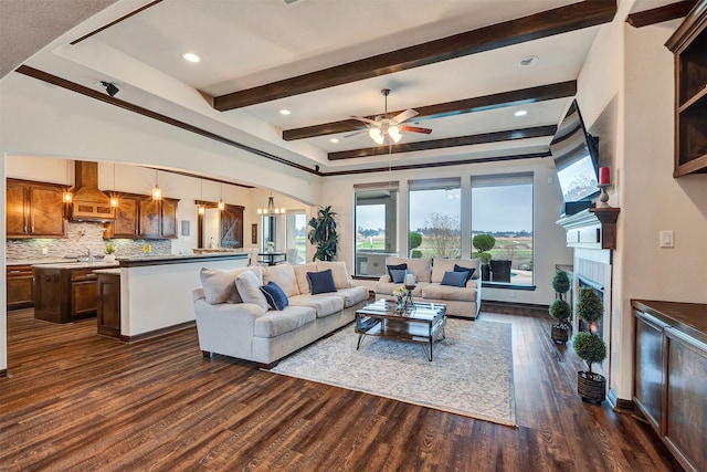 living room with ceiling fan with notable chandelier, arched walkways, dark wood-style flooring, a warm lit fireplace, and beam ceiling