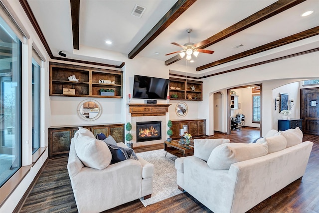 living area featuring a glass covered fireplace, dark wood-style flooring, beam ceiling, visible vents, and arched walkways