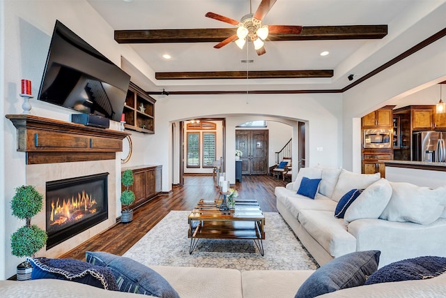 living area featuring a glass covered fireplace, arched walkways, beamed ceiling, stairs, and dark wood-style flooring