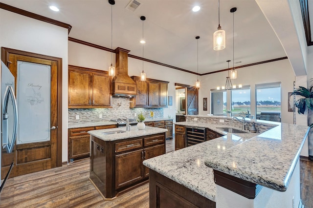 kitchen featuring a sink, a spacious island, decorative light fixtures, custom exhaust hood, and visible vents