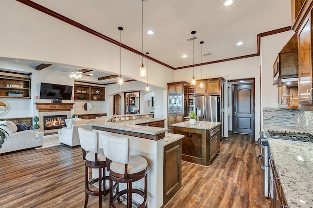 kitchen featuring light stone countertops, appliances with stainless steel finishes, pendant lighting, an island with sink, and open floor plan