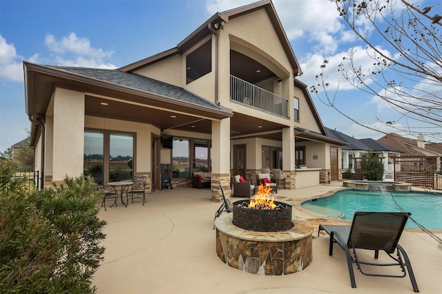 back of house with stucco siding, a fire pit, fence, a pool with connected hot tub, and a balcony