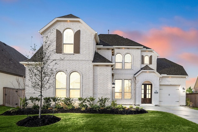 french country inspired facade featuring a garage, concrete driveway, brick siding, and a yard