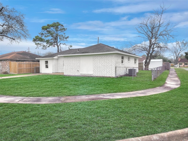 view of side of property with central air condition unit, brick siding, fence, a yard, and roof with shingles