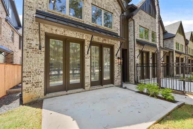 entrance to property with brick siding, french doors, a patio, and fence