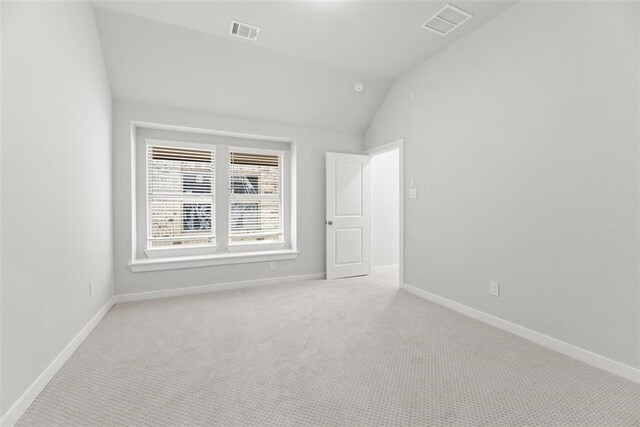 empty room featuring visible vents, lofted ceiling, light colored carpet, and baseboards