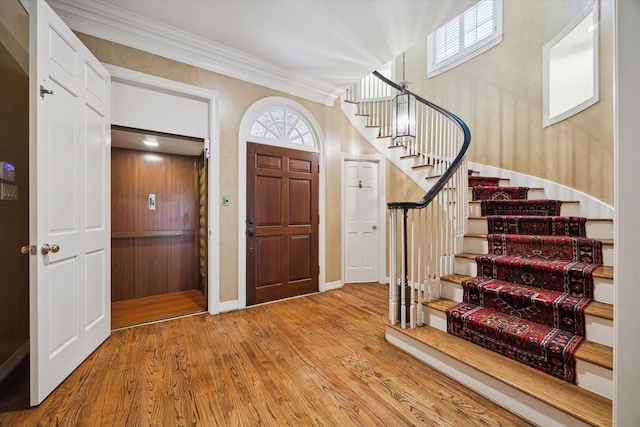 entrance foyer with elevator, crown molding, stairs, and wood finished floors