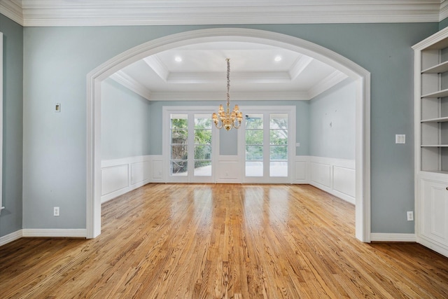 unfurnished dining area featuring ornamental molding, a raised ceiling, built in shelves, and light wood finished floors