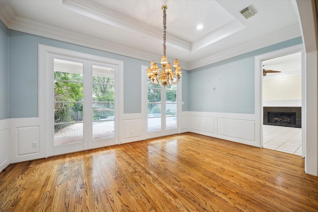 unfurnished dining area featuring a fireplace, wood finished floors, visible vents, ornamental molding, and a tray ceiling