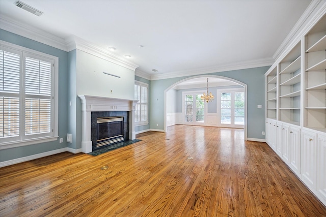 unfurnished living room with a premium fireplace, visible vents, wood finished floors, and ornamental molding