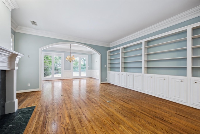 unfurnished living room with a chandelier, arched walkways, wood finished floors, visible vents, and crown molding