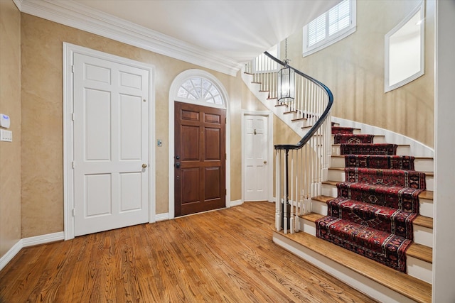 foyer with stairway, ornamental molding, wood finished floors, plenty of natural light, and baseboards