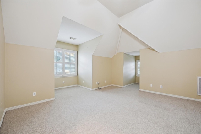 additional living space with light carpet, baseboards, visible vents, and vaulted ceiling