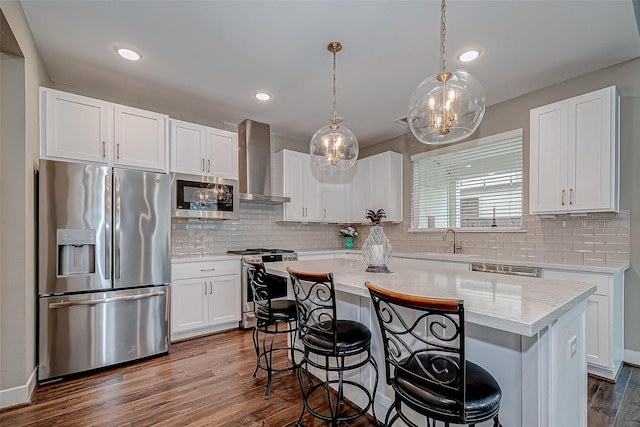 kitchen with white cabinets, wall chimney exhaust hood, a kitchen island, appliances with stainless steel finishes, and a sink