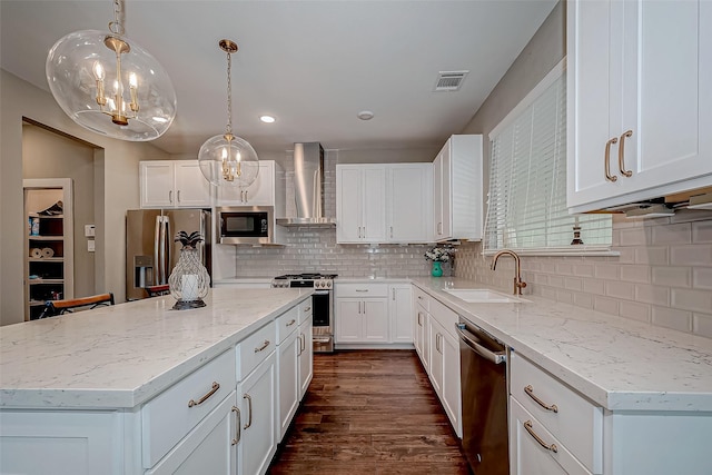 kitchen featuring white cabinetry, hanging light fixtures, appliances with stainless steel finishes, a center island, and wall chimney exhaust hood