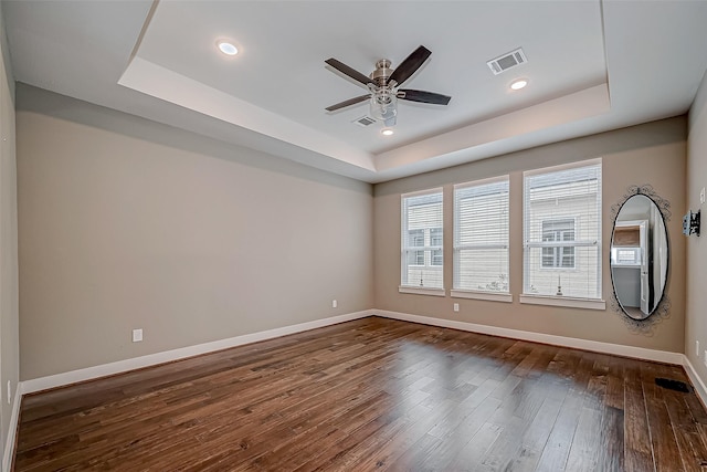 spare room with dark wood-type flooring, a raised ceiling, and visible vents