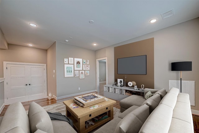 living room with recessed lighting, visible vents, baseboards, and wood finished floors