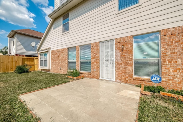 view of exterior entry with fence, brick siding, a patio area, and a yard