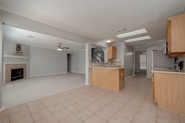 kitchen with open floor plan, light brown cabinets, visible vents, a tiled fireplace, and a peninsula