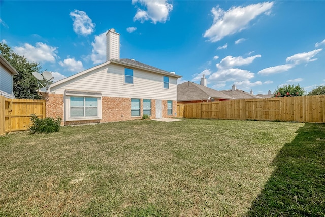 back of property with brick siding, a fenced backyard, a yard, and a chimney