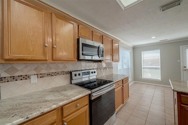 kitchen with light tile patterned floors, stainless steel appliances, ornamental molding, visible vents, and light stone counters