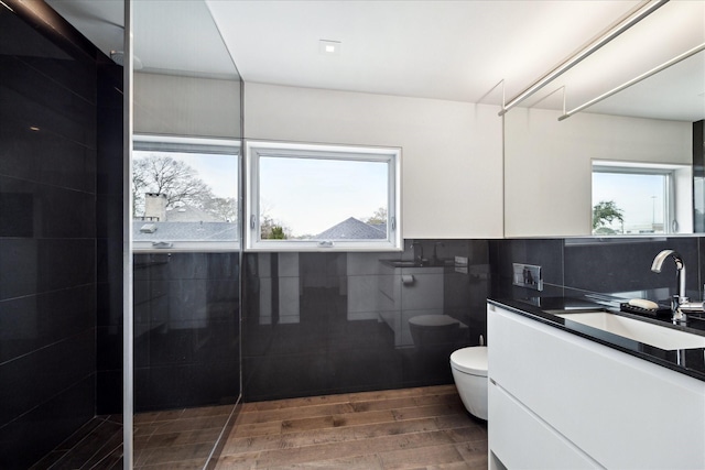 bathroom featuring toilet, tile walls, vanity, wood finished floors, and walk in shower