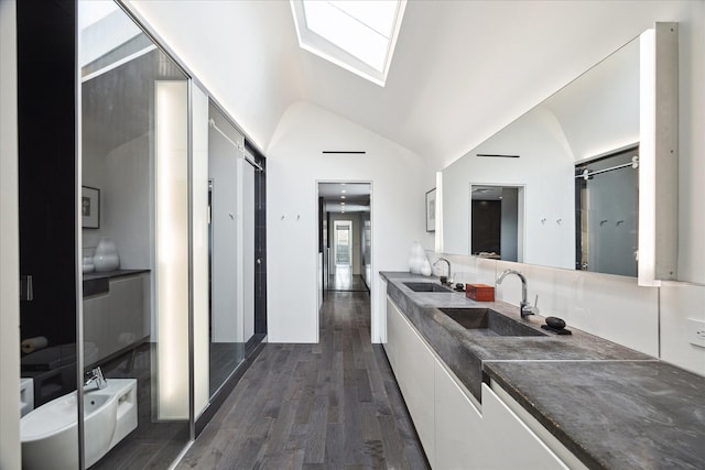 full bath with double vanity, vaulted ceiling with skylight, wood finished floors, and a sink