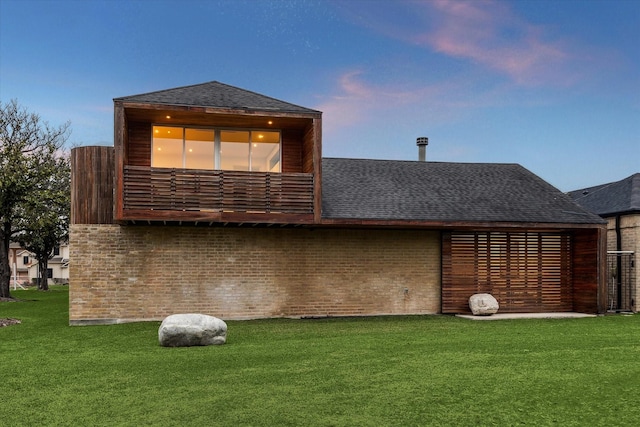 back of house at dusk featuring roof with shingles and a yard