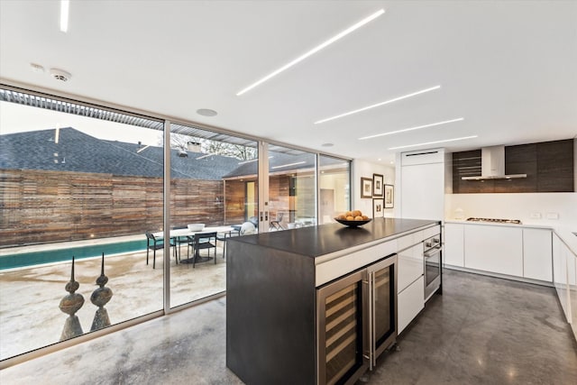 kitchen with white cabinetry, beverage cooler, wall chimney exhaust hood, concrete flooring, and modern cabinets