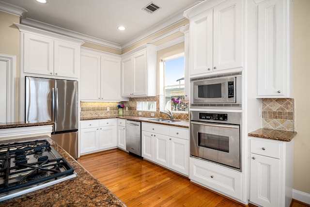 kitchen featuring visible vents, white cabinetry, a sink, dark stone countertops, and appliances with stainless steel finishes