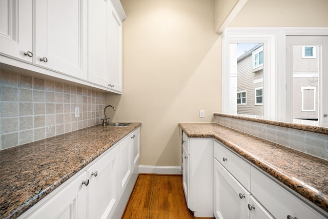 kitchen featuring dark stone countertops, dark wood-type flooring, white cabinets, and a sink