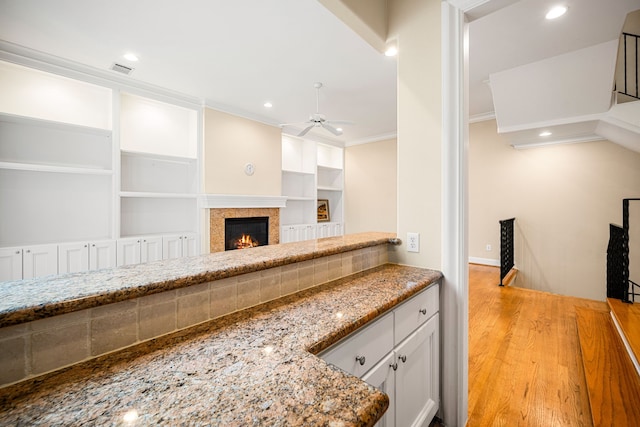 kitchen featuring stone countertops, ceiling fan, crown molding, and light wood-type flooring