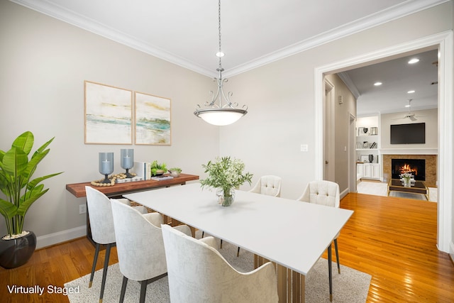 dining space with baseboards, crown molding, light wood-style floors, recessed lighting, and a lit fireplace