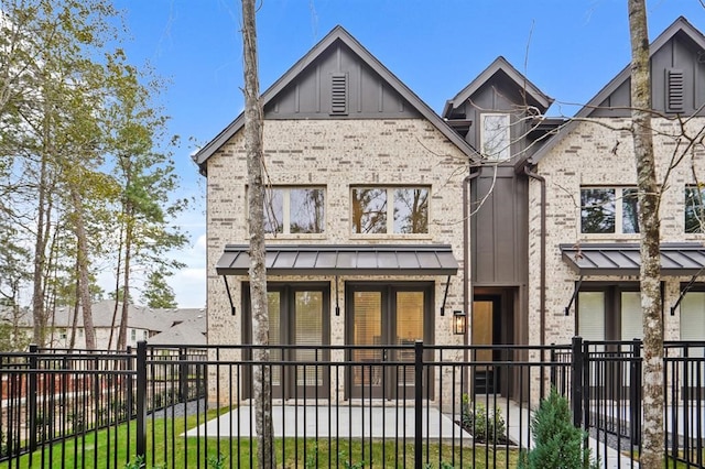 view of front of house featuring brick siding, metal roof, a fenced front yard, a front yard, and a standing seam roof